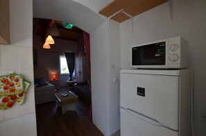 A compact kitchen with a microwave oven on top of a refrigerator, a small dining table, and a window with curtains.