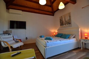 A bedroom with a bed, a chair, a TV, and a painting on the wall.