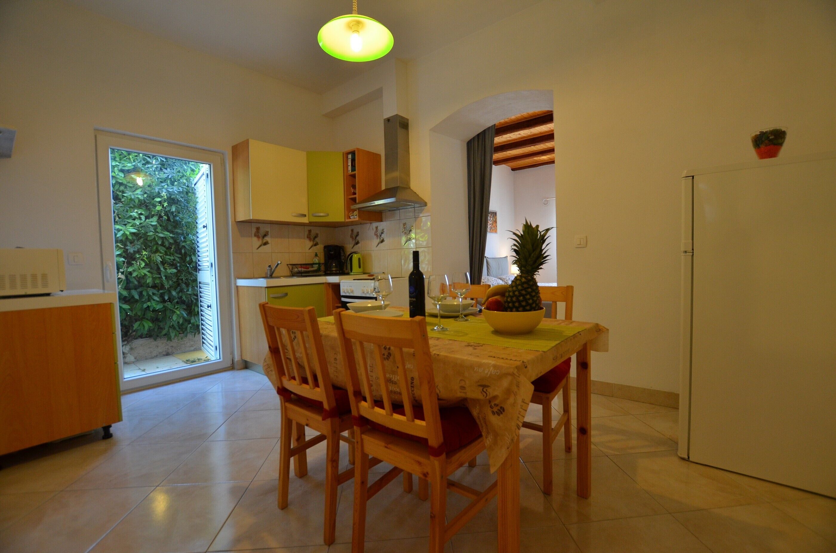 A dining area with a table set for two, wooden chairs, a bowl of fruit, and a bottle of wine.