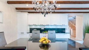 A modern kitchen with white cabinets, a central island with a fruit bowl, and a chandelier. - Villa Fema Royal with wheerpool and sea view (Rovinj)