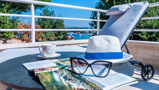 A lounge chair with a cushion, a hat, a cup, and a magazine on a table with a view of the sea and boats. - Villa Fema Royal with wheerpool and sea view (Rovinj)