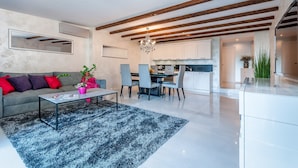 A modern living room with a sofa, coffee table, and chairs. There is a kitchen in the background with cabinets and a chandelier. - Villa Fema Royal with wheerpool and sea view (Rovinj)
