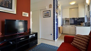 A living room with a TV, a red sofa, and a kitchen area with white cabinets and blue tiles. - Alma Borik Apartment with balcony (Rovinj)