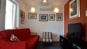A living room with a red sofa, a striped chair, a flat-screen TV, and framed artwork on the walls. - Alma Borik Apartment with balcony (Rovinj)
