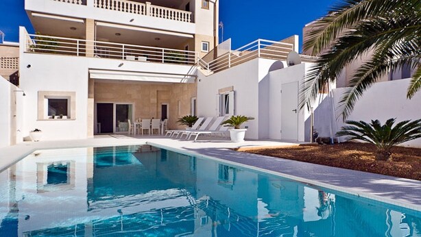 A swimming pool with lounge chairs, a building with balconies, and a palm tree.