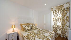A bedroom with a bed, two bedside tables, a nightstand, a door, and a patterned curtain.
