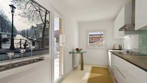A narrow kitchen with a view of a canal, a small table with a vase, and a window with a view of a building.