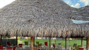 A covered outdoor seating area with thatched umbrellas, tables, and chairs.