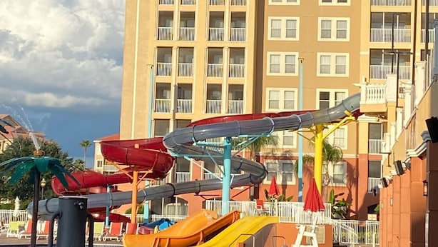 A swimming pool area with water slides and a building with balconies in the background.