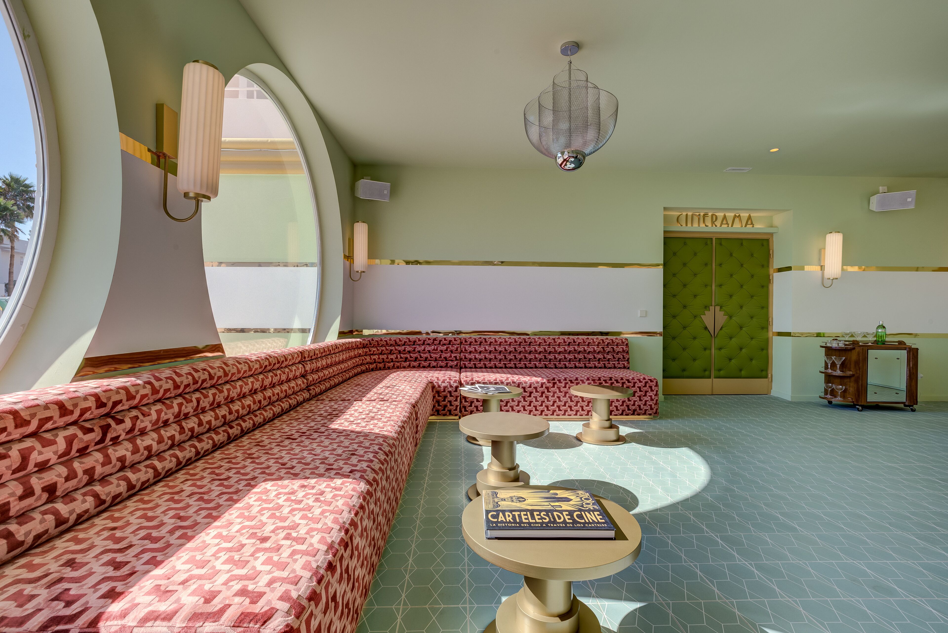 A modern interior with a curved seating area, a green door labeled "CINEMA," and a table with a book titled "Carteles de Cine."
