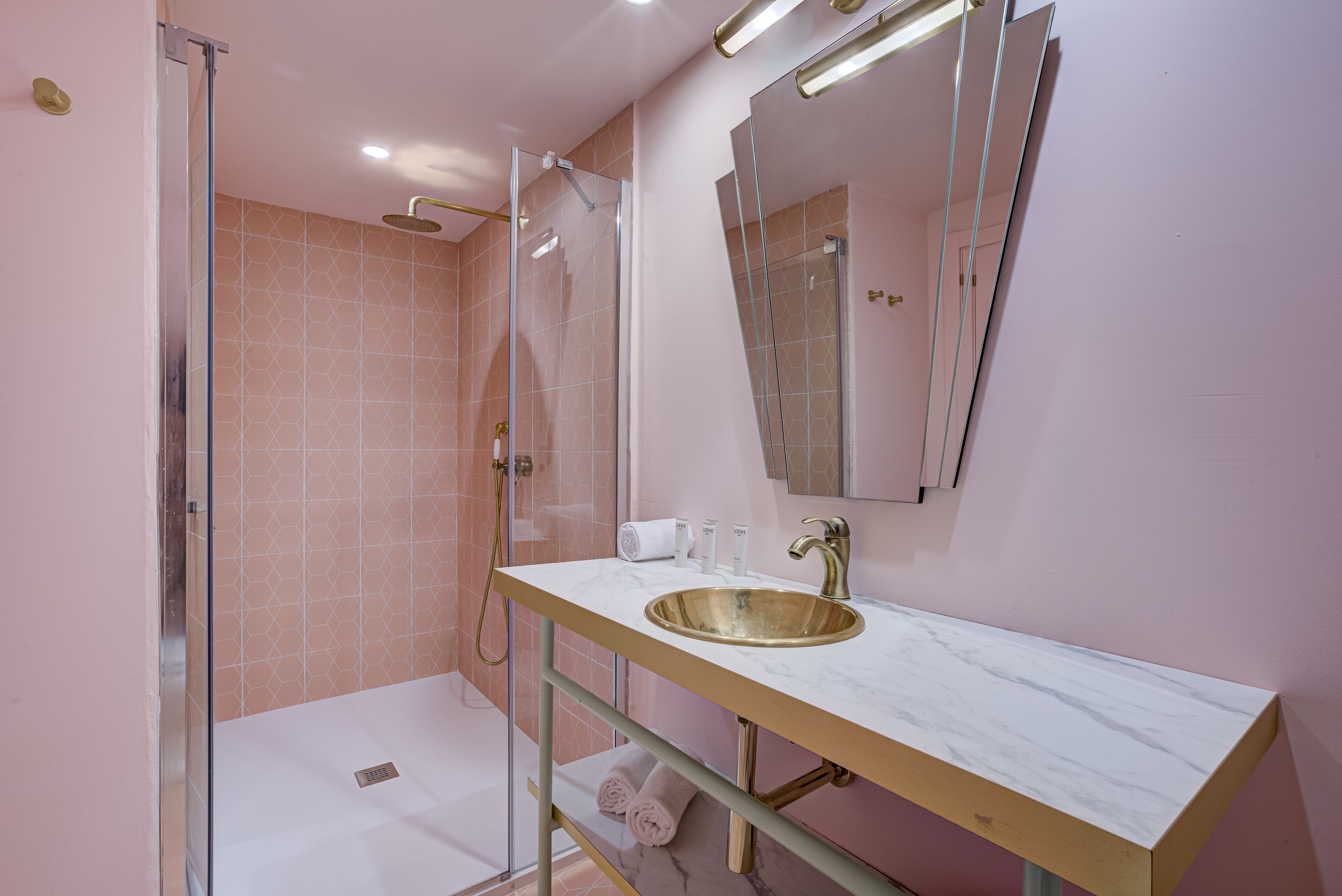 A modern bathroom with a glass-enclosed shower, a gold sink, and a large mirror.