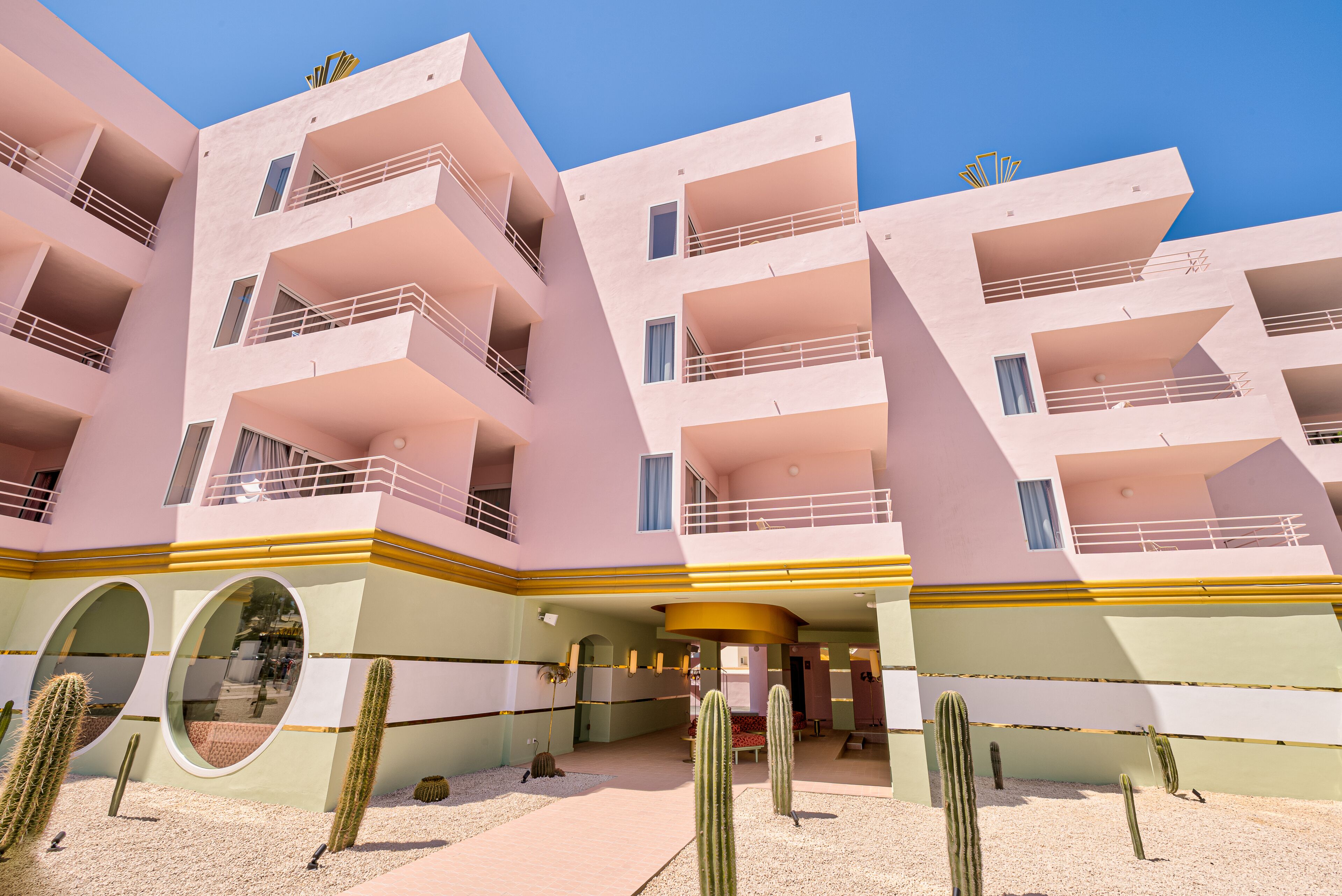 A multi-story building with balconies, a courtyard with cacti, and a clear blue sky.