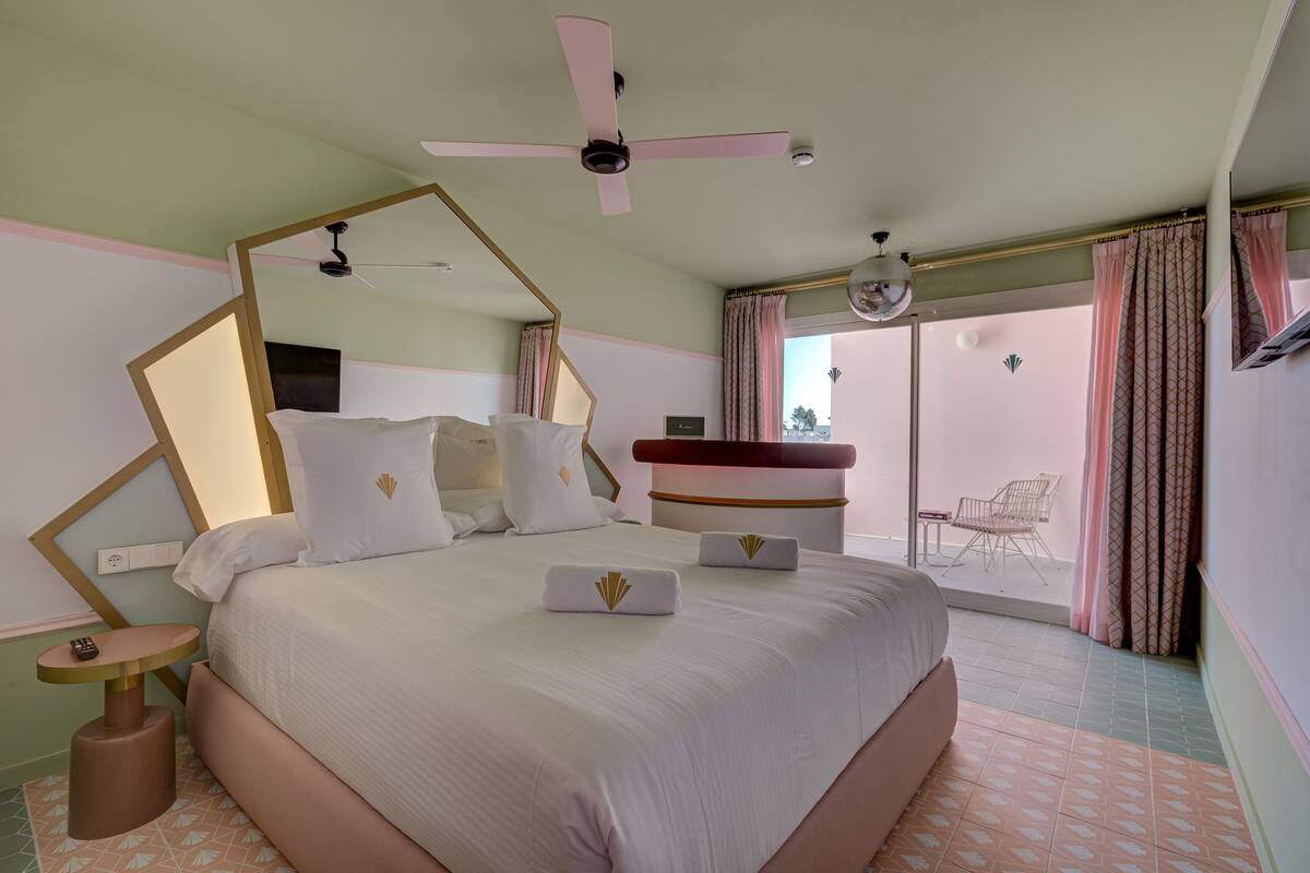 Quarto bem arrumado com cama, mesas de cabeceira, ventilador de teto e vista para o exterior.