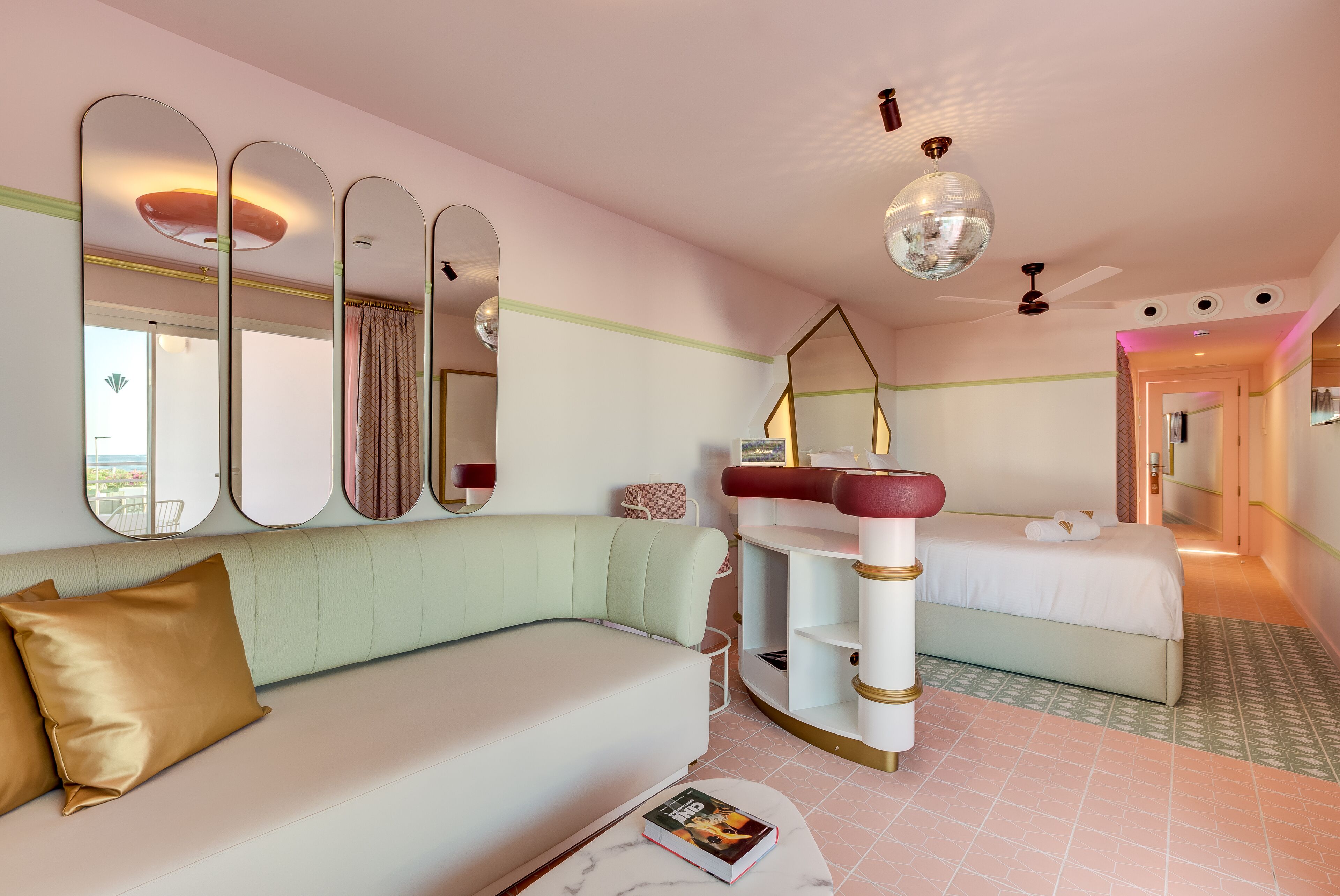 A modern hotel room with a sofa, a bed, a vanity with mirrors, and a ceiling fan.