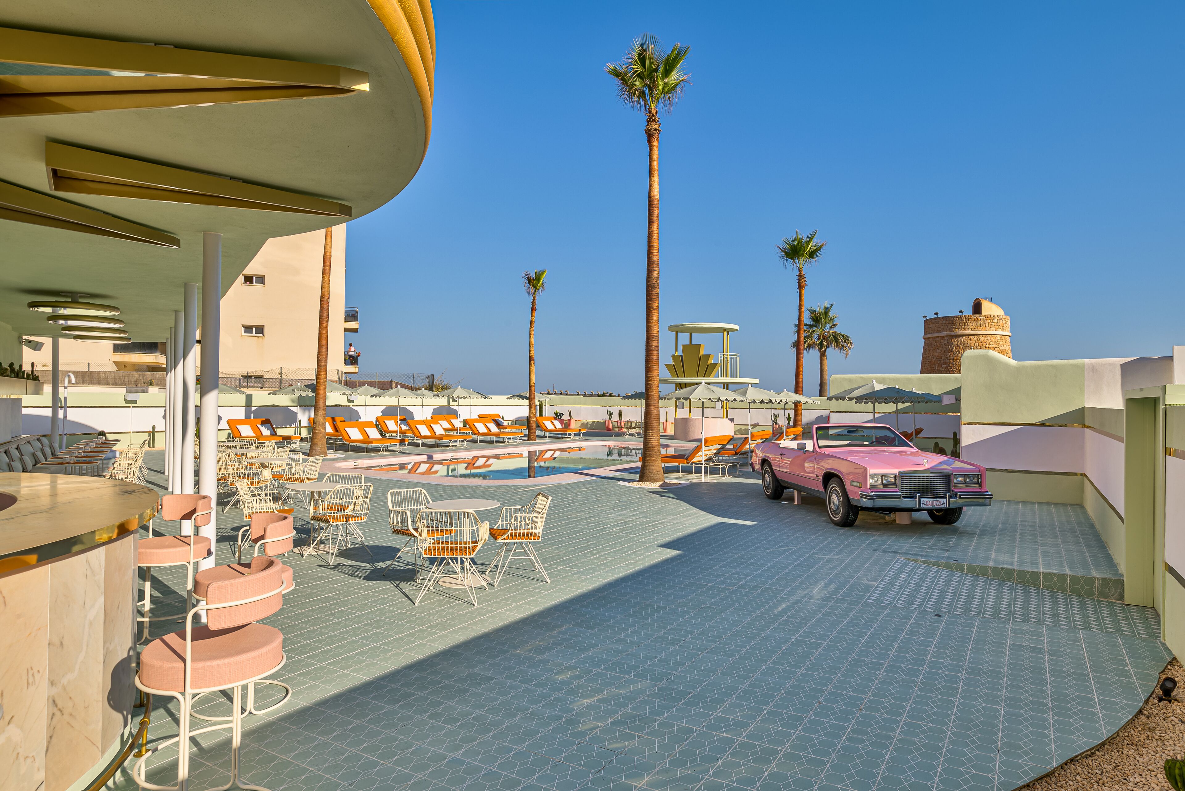 A rooftop bar with outdoor seating, a pink car, and palm trees.