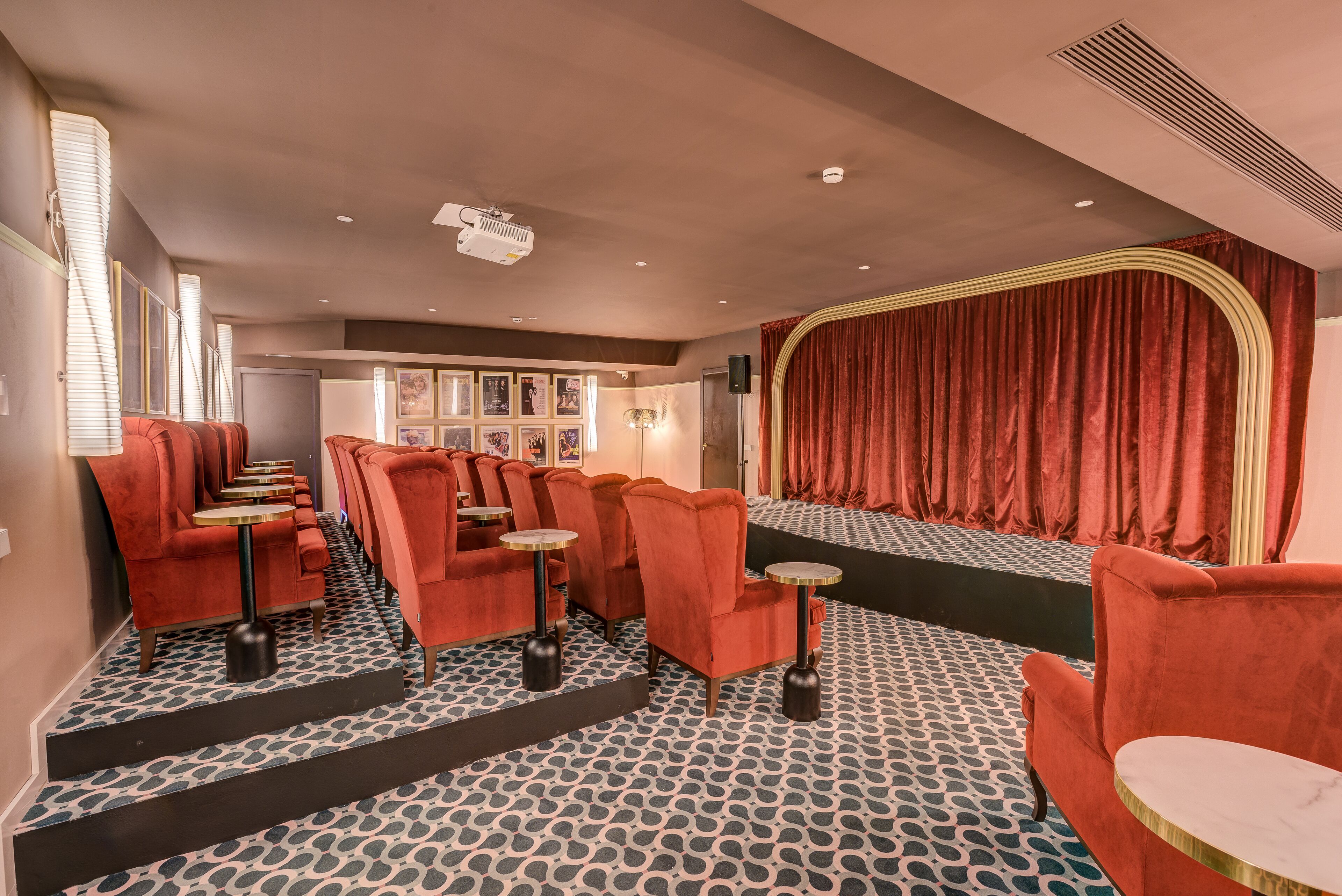 A cinema with red velvet curtains, a patterned carpet, and rows of red velvet seats.