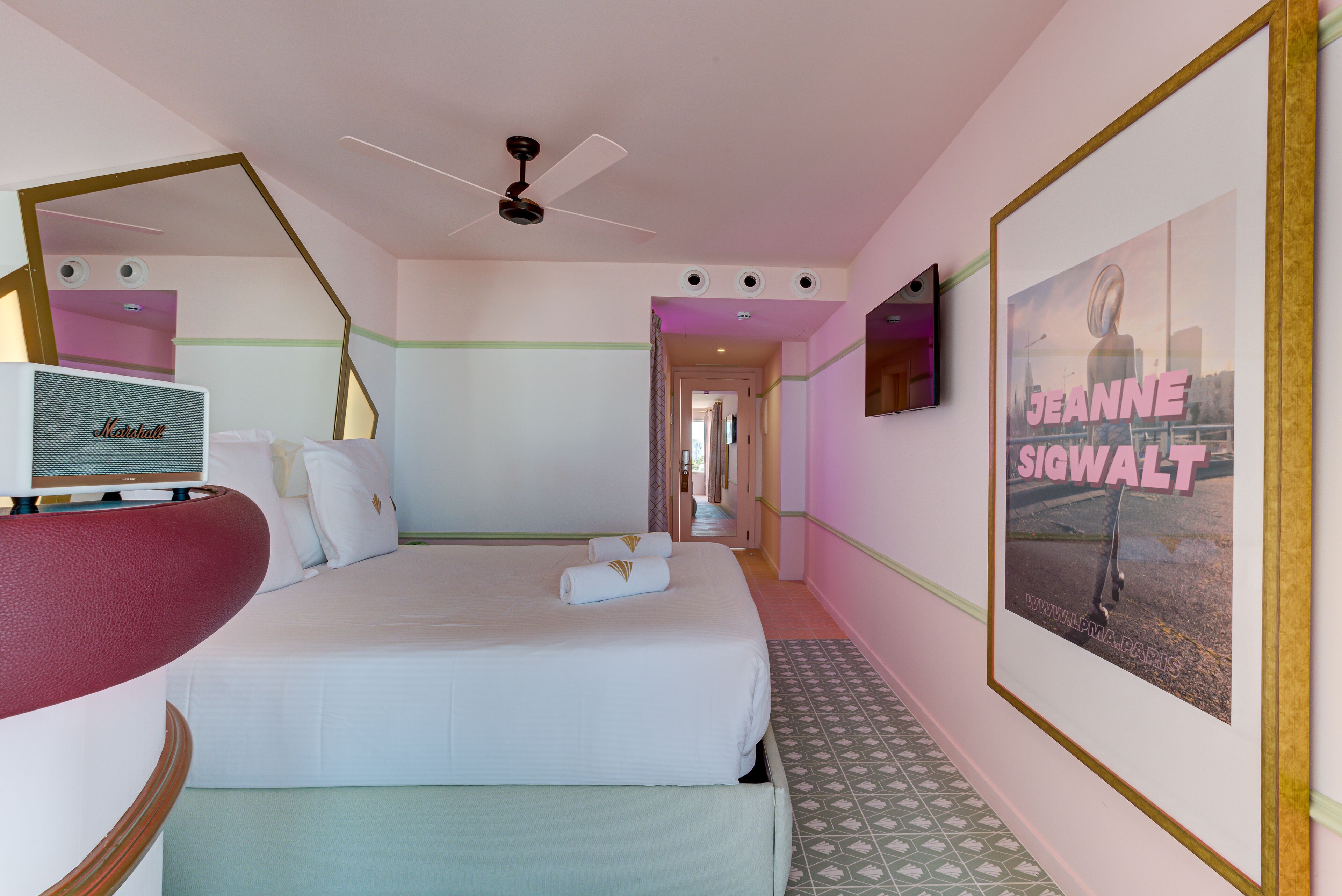 A hotel room with a bed, a ceiling fan, a television, and a framed poster on the wall.