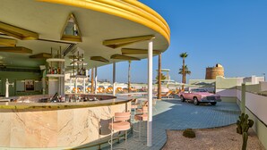 A modern bar area with a marble counter, bar stools, and a vintage car parked outside.