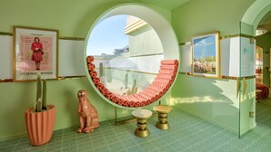A room with a circular mirror, a cactus, a lion statue, and framed pictures on the walls.