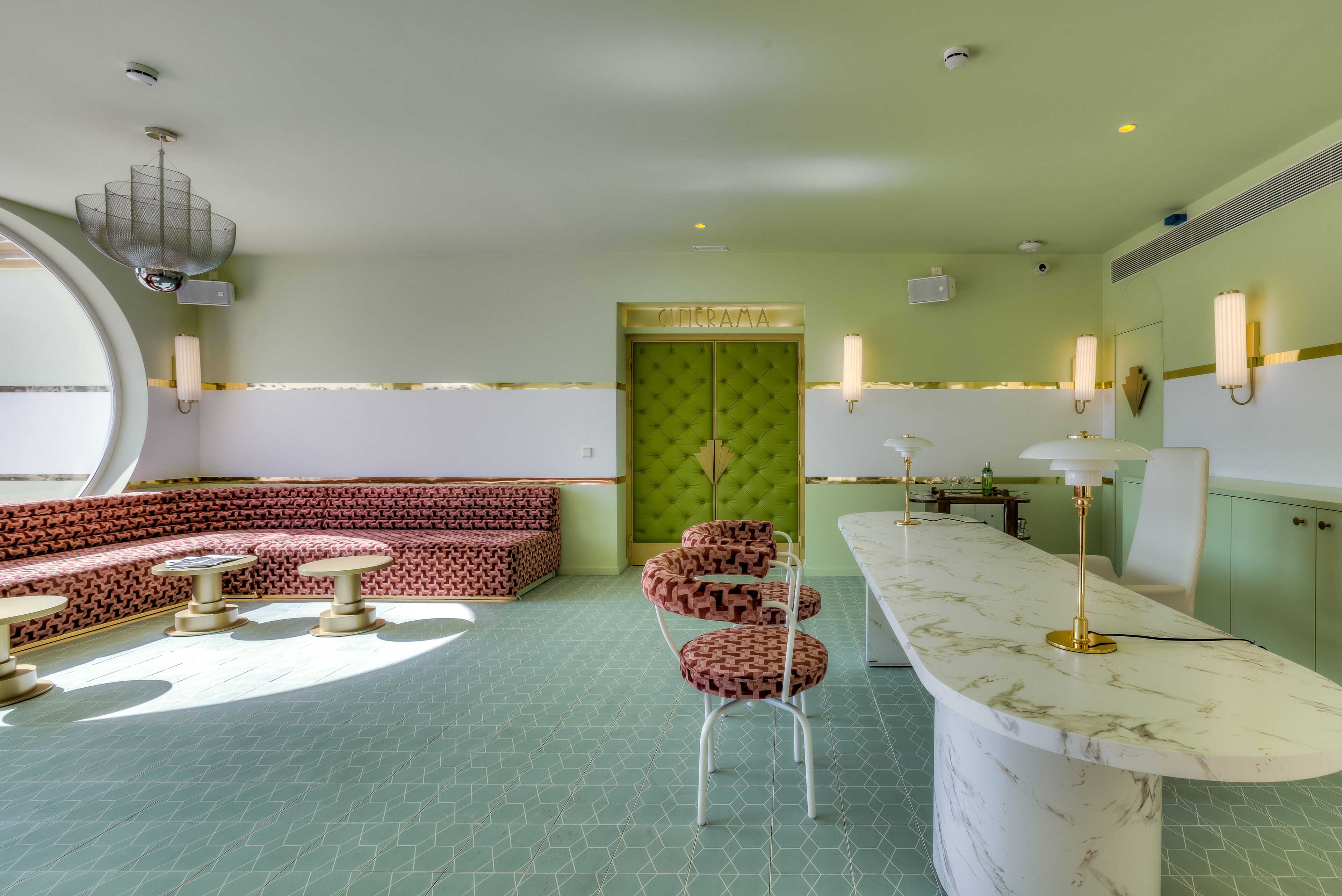 Une pièce avec un mur vert, une porte verte à motifs, une table ronde et un coin bar doté d’un comptoir en marbre.