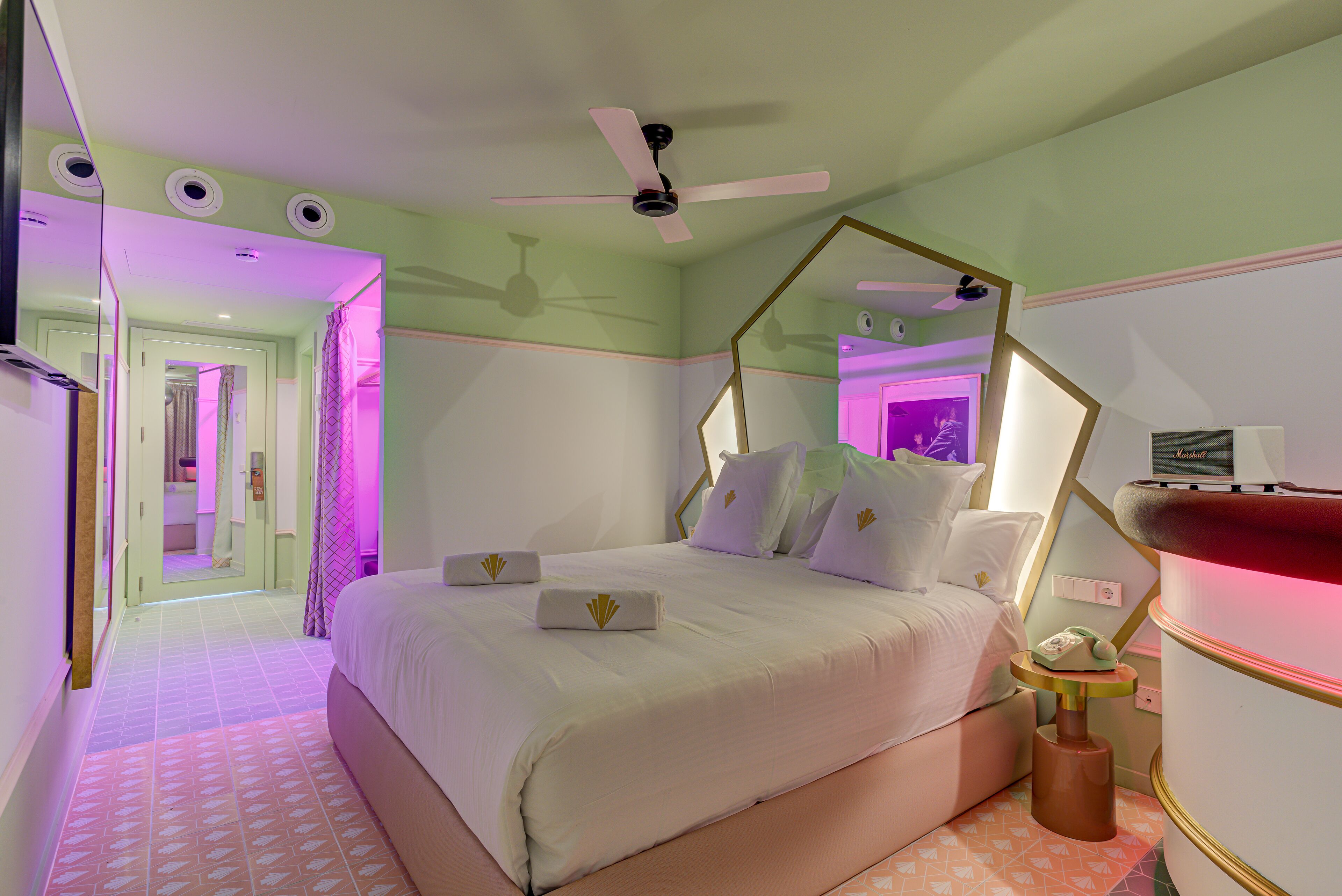 Una habitación de hotel moderna con una cama grande, un ventilador de techo, una mesita de noche y un espejo.
