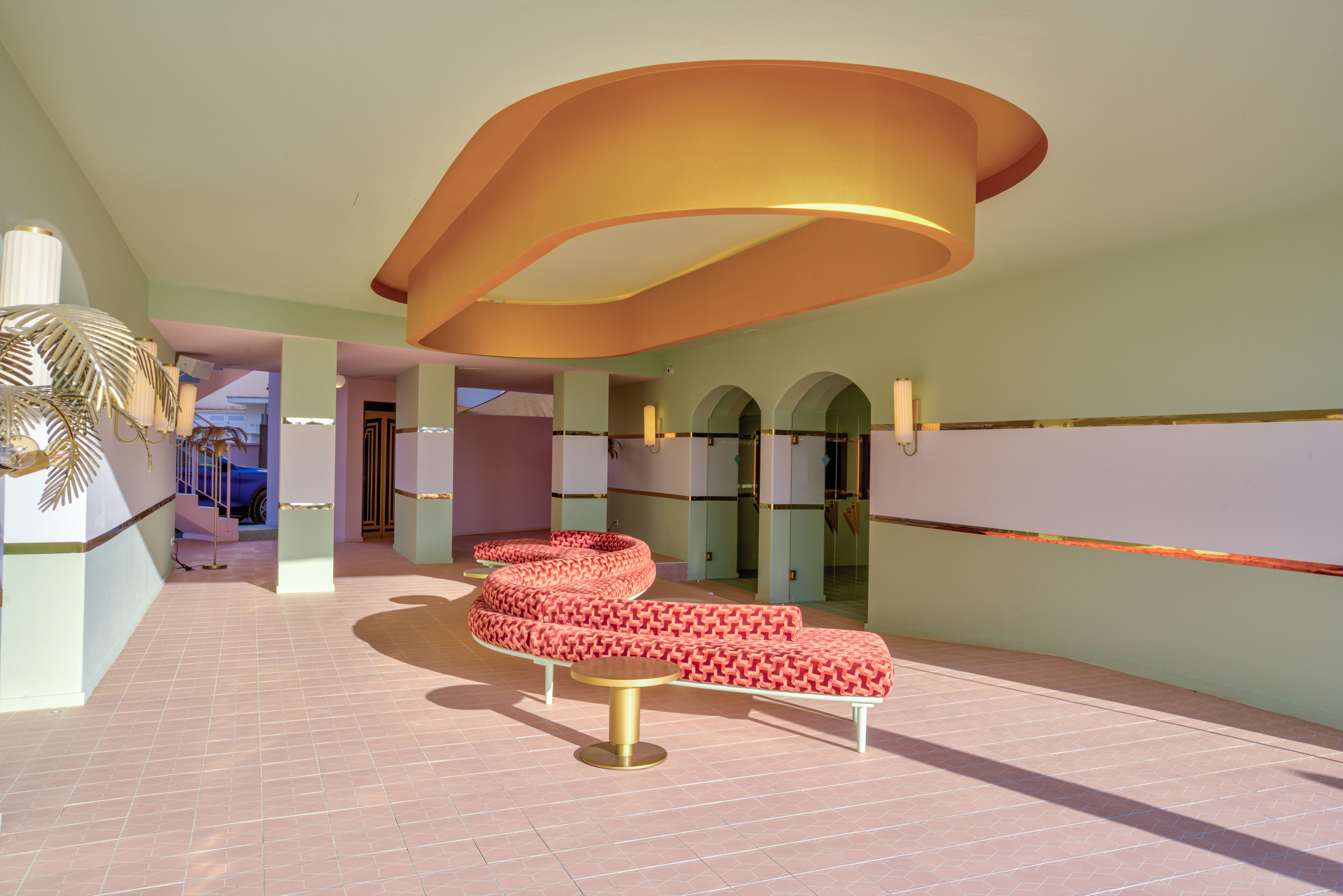 A modern lobby with a curved ceiling, a seating area with patterned cushions, and a palm tree decoration.