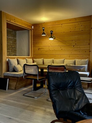 A cozy room with a wooden wall, a stone accent wall, a wooden table with chairs, and a bench with cushions. - Apartment 100 m2 Megève Centre near Church -Skis at feet (Megève)