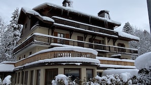 Un immeuble à plusieurs étages doté de balcons, entouré d’arbres et d’arbustes couverts de neige.