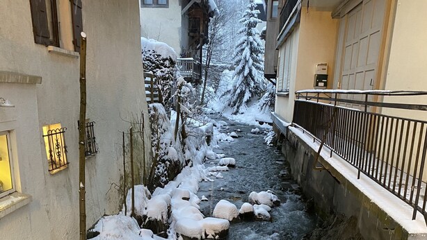 Un petit ruisseau étroit, recouvert de neige, traverse un quartier résidentiel bordé de maisons des deux côtés.