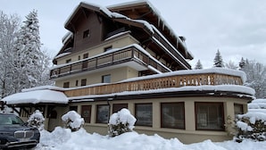 Un immeuble à plusieurs étages, doté de balcons recouverts de neige, entouré d’arbres également couverts de neige.