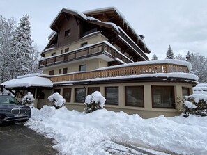 Um edifício de vários andares com varandas cobertas de neve, rodeado por árvores carregadas de neve.