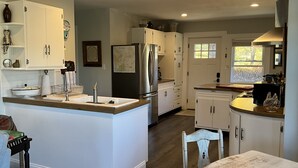 Une cuisine moderne avec des meubles blancs, un réfrigérateur en acier inoxydable et un îlot central en bois doté d’un évier.
