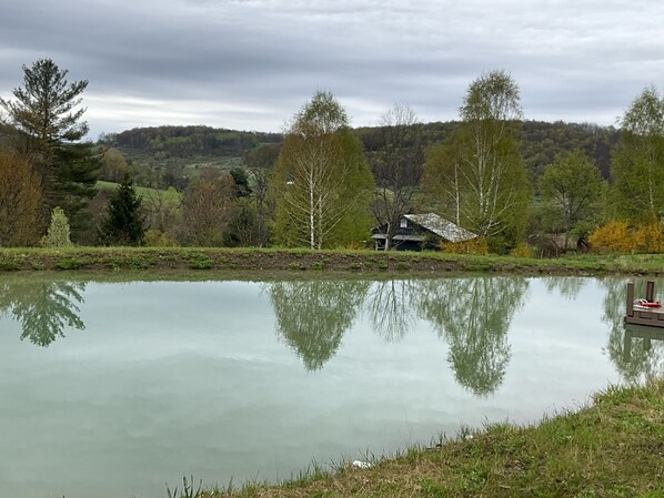 Un lac paisible, avec un quai en bois et un chalet rustique entouré d’arbres.