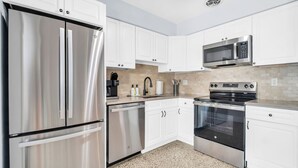 A modern kitchen with stainless steel appliances, white cabinetry, and a tiled backsplash.