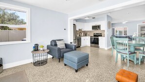 A modern kitchen with white cabinets, a dining area with teal chairs, and a grey sofa.