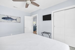 Un dormitorio con una cama grande, un ventilador de techo, un televisor montado y una puerta que da a otra habitación.