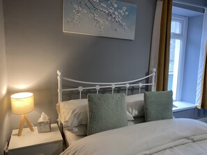 Cozy retreat with a white bed, bedside table, and artwork above, offering a peaceful view from the window.