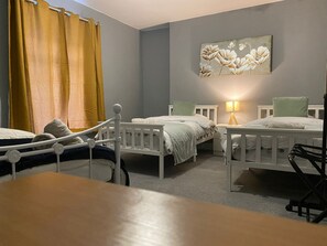 Two single beds with white frames and green bedding, a nightstand with a lamp, and a floral painting adorn this inviting bedroom.