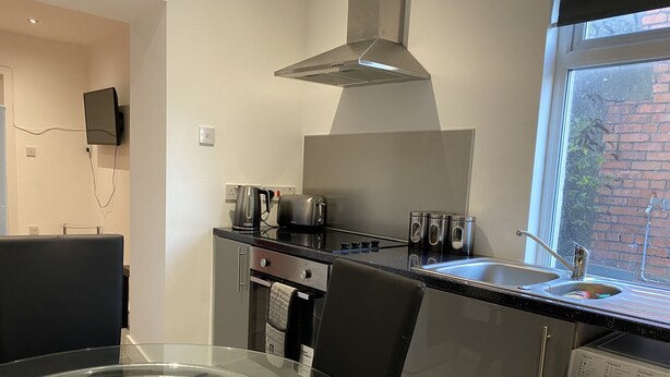 A modern kitchen with a stainless steel range hood, a coffee maker, a toaster, and a built-in washing machine. - Bridgend Central 2-bed Apartment (Bridgend)