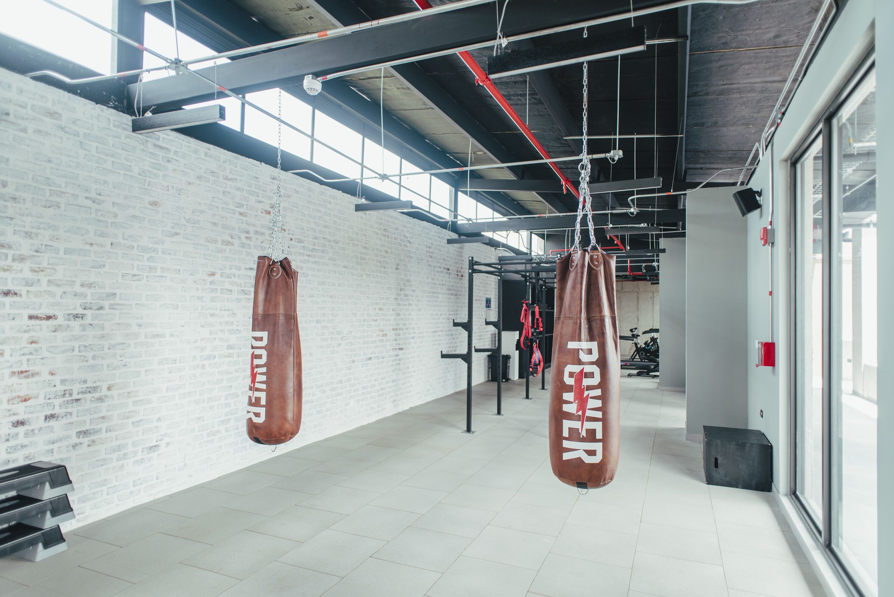 A gym with white brick walls, large windows, and hanging punching bags labeled "POWER".
