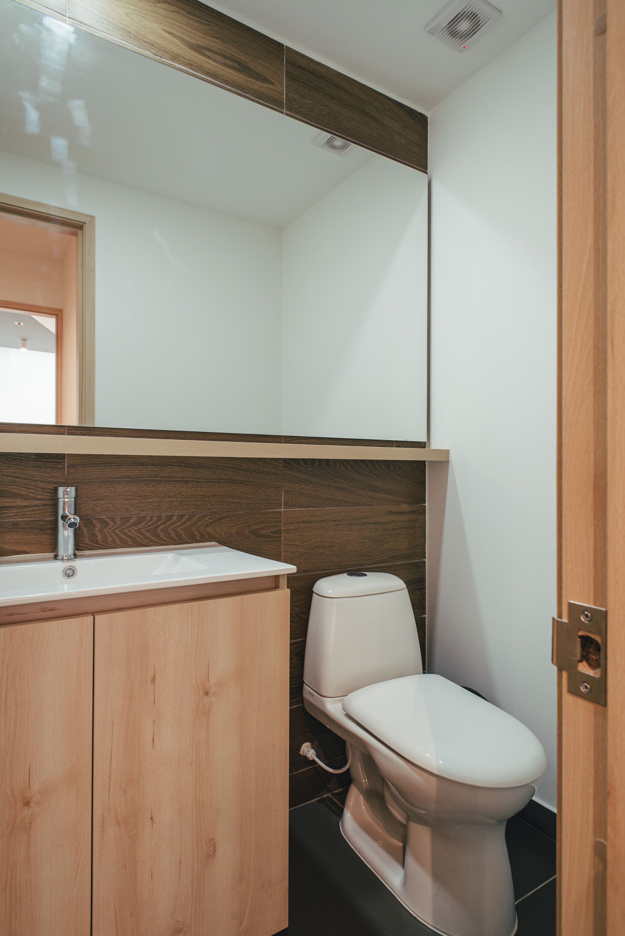 A modern bathroom with a wooden vanity, a white sink, and a toilet.