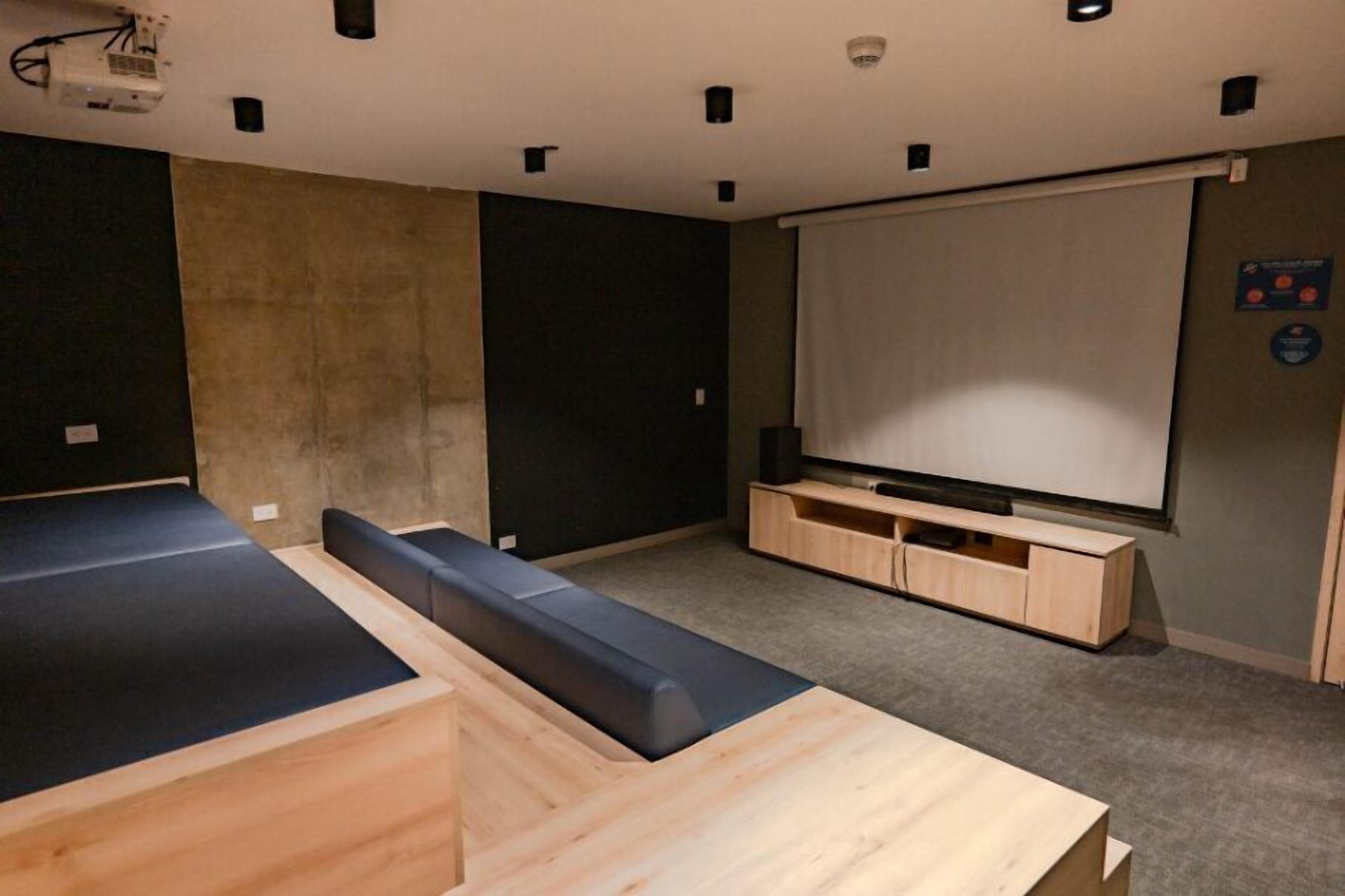A modern room with a large flat-screen TV, a wooden bench, and a projector mounted on the ceiling.