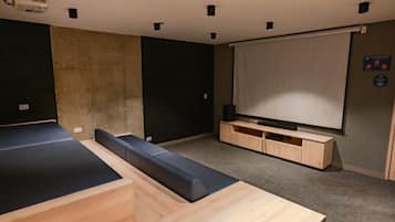 A modern room with a large flat-screen TV, a wooden bench, and a projector mounted on the ceiling.