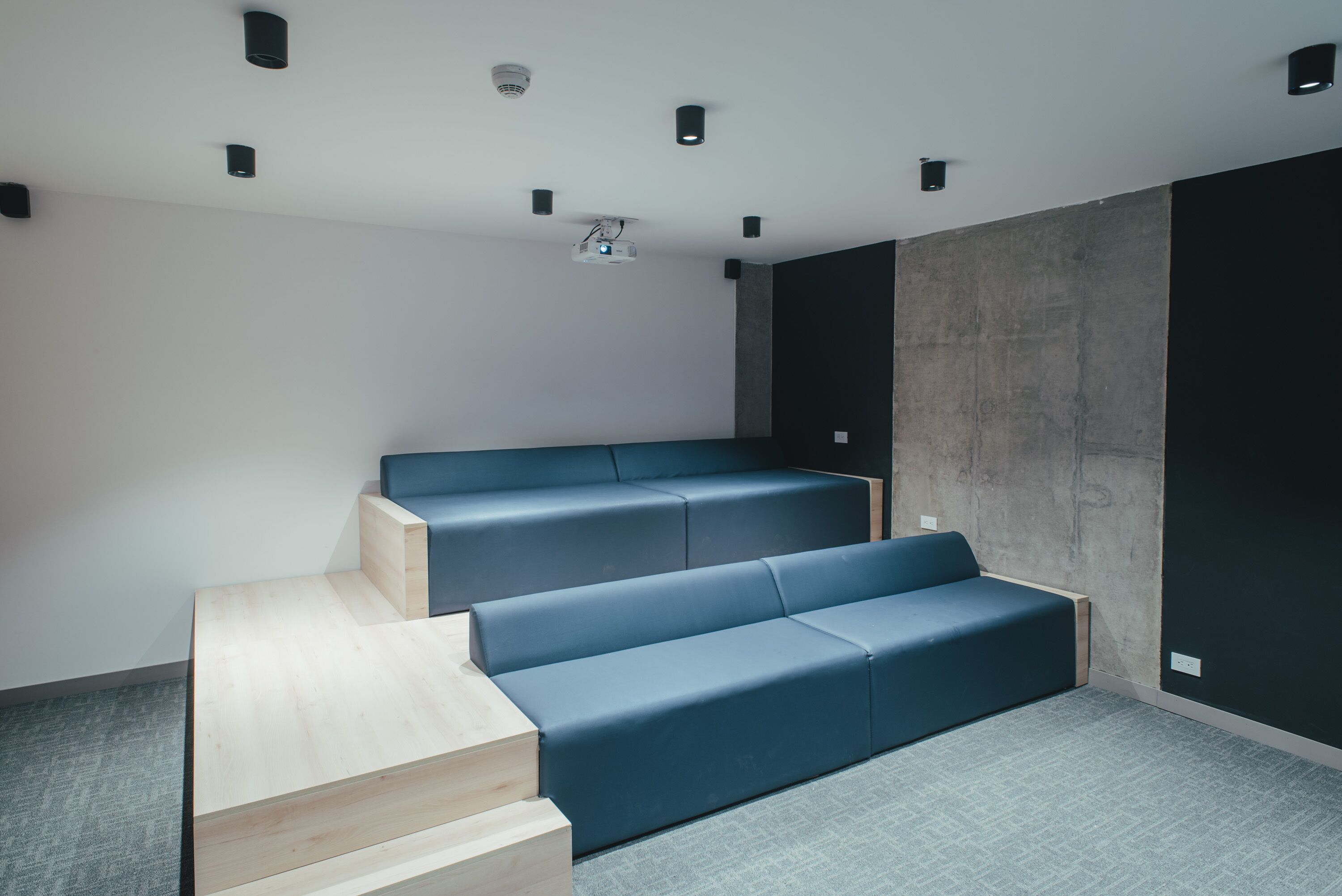 A modern cinema room with tiered seating and a projector.