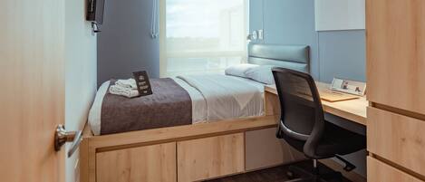 A compact bedroom with a bed, a desk, and a chair.