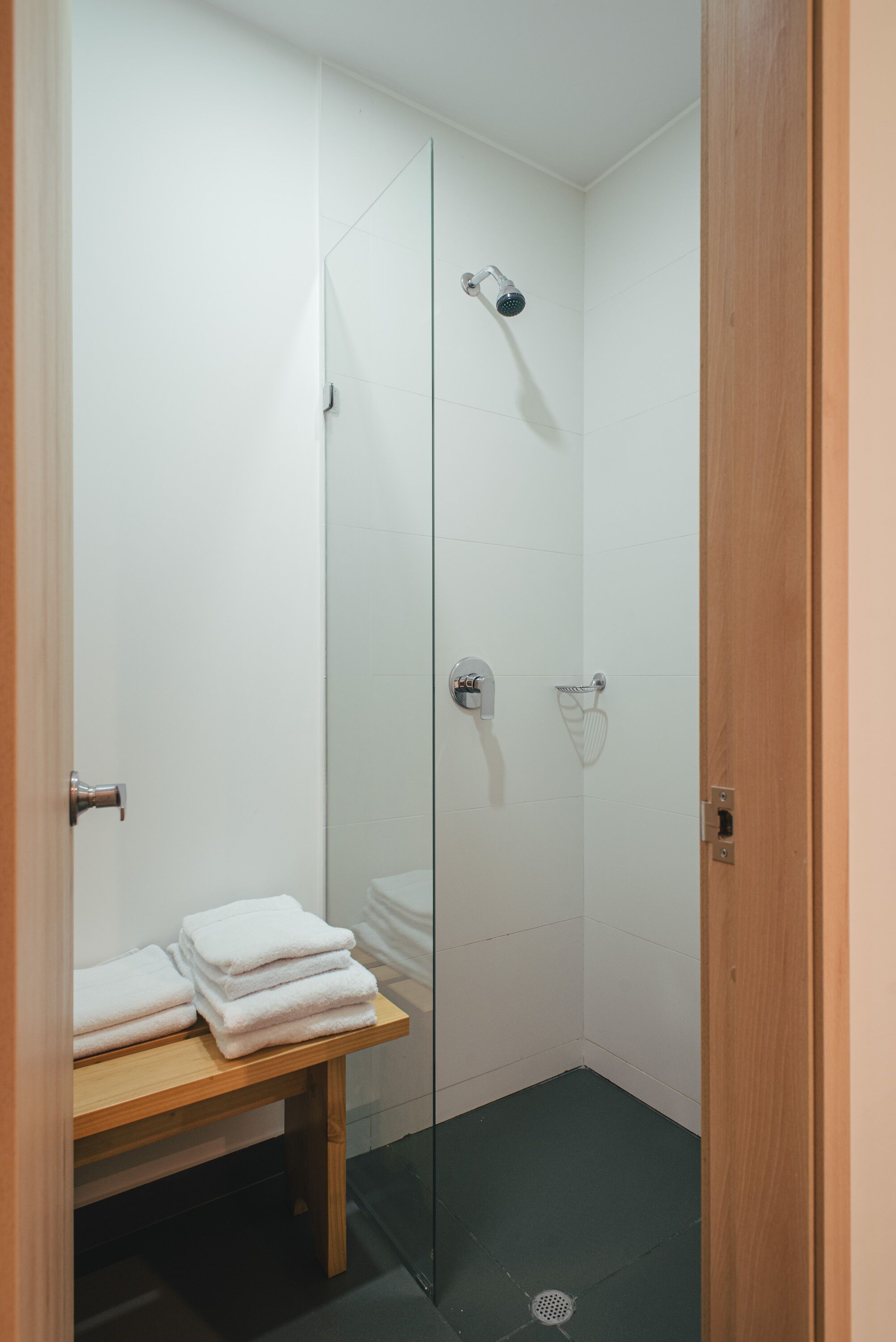 A glass-enclosed shower with a handheld showerhead, a towel rack, and a bench with towels.