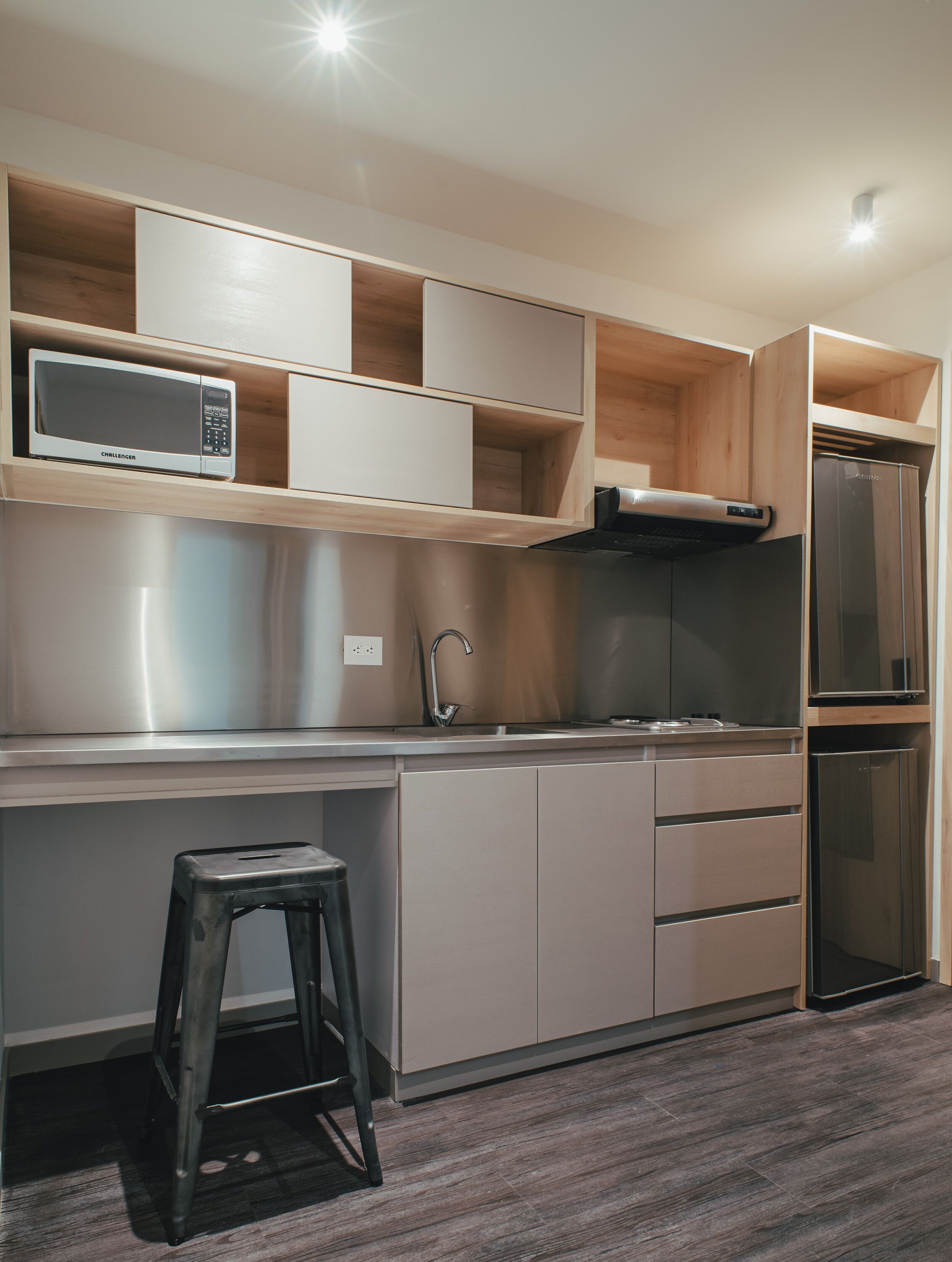Cocina compacta equipada con microondas, refrigerador y un taburete.