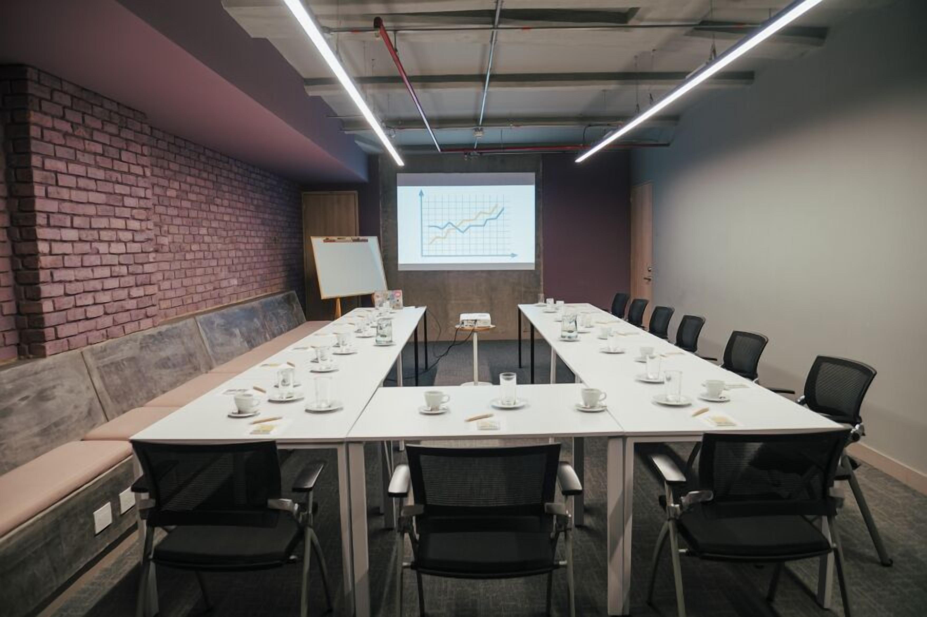Una sala de conferencias con una larga mesa, sillas, una pantalla de proyector y una pizarra.