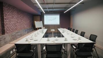 Una sala de conferencias con una larga mesa, sillas, una pantalla de proyector y una pizarra.