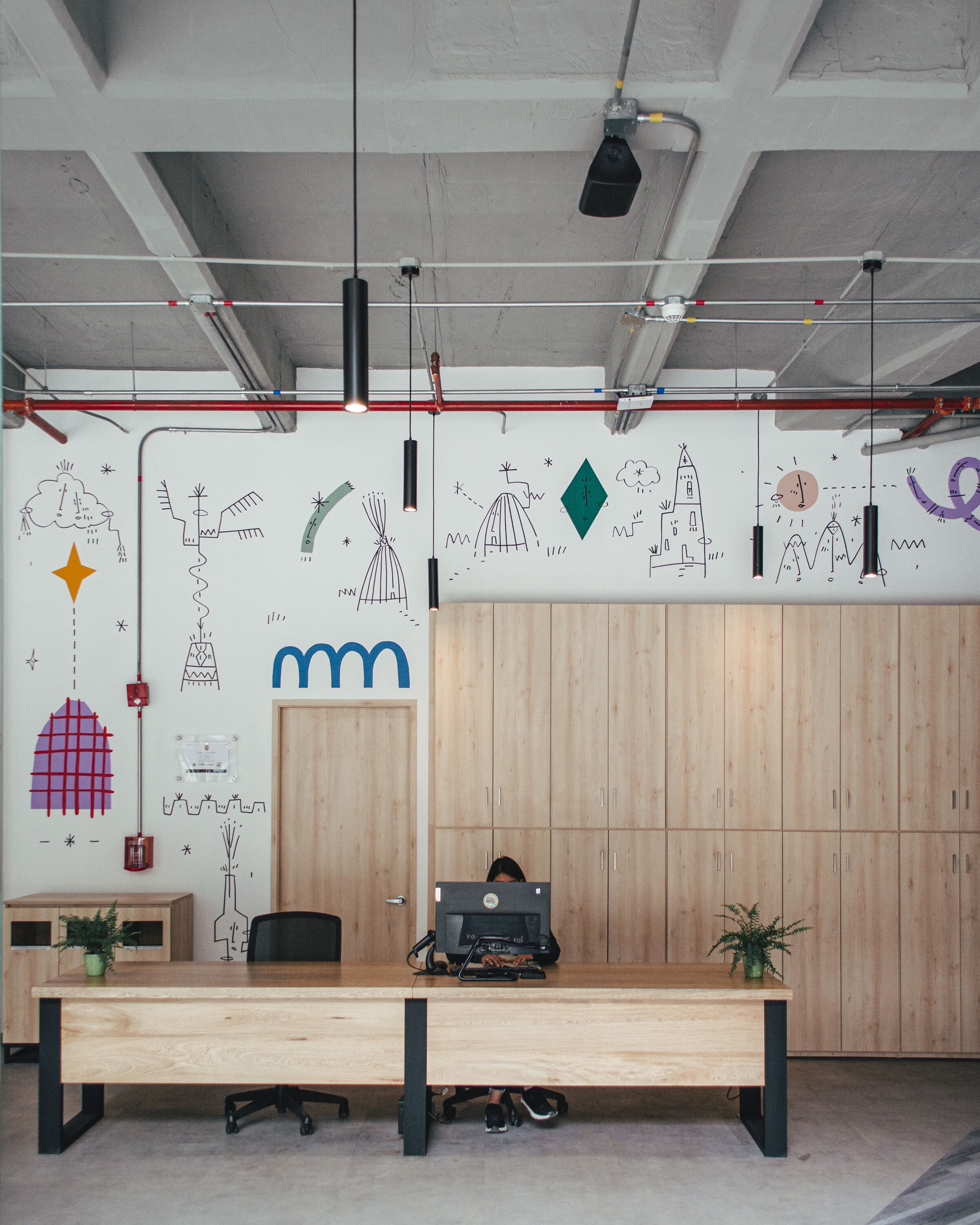 A modern office space with a wooden desk, a computer, and a wall decorated with abstract drawings.